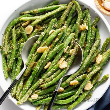 Roasted green beans in a bowl with serving spoons.